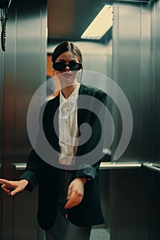 Stylish woman in black jacket and sunglasses posing in elevator, fashion model, dark cinematic light and color