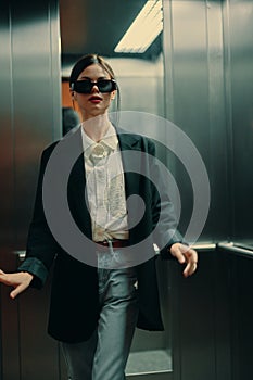 Stylish woman in black jacket and sunglasses posing in elevator, fashion model, dark cinematic light and color