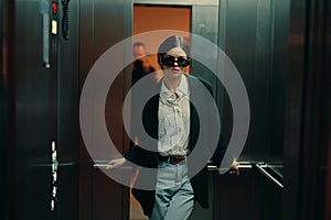 Stylish woman in black jacket and sunglasses posing in elevator, fashion model, dark cinematic light and color, glamor