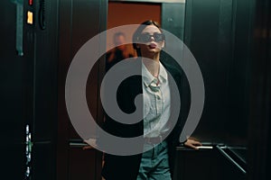 Stylish woman in black jacket and sunglasses posing in elevator, fashion model, dark cinematic light and color, glamor