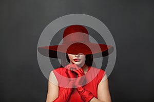 Stylish woman brunette with makeup and dark hair wearing red dress and red silk gloves and red wide broad brim hat on black