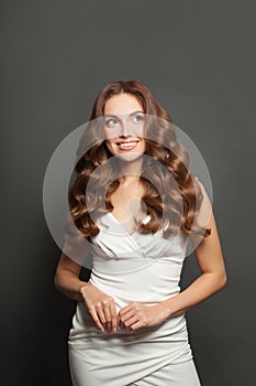 Stylish woman brunette model with long wavy brown hair wearing white dress looking up on black background