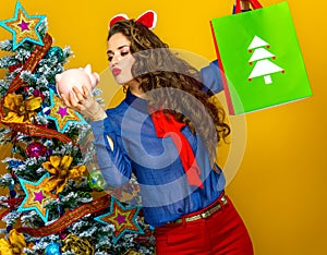 Stylish woman with Christmas shopping bag and piggy bank