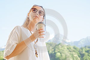 Stylish woman with cup of coffee on background of summer mountains.