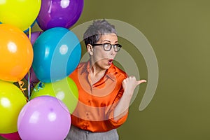 Stylish woman with glasses pointing emphatically while surrounded by colorful balloons in a festive environment with photo