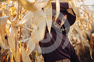 Stylish woman in hat and brown clothes posing in autumn maize field in warm sunny light. Portrait of fashionable attractive young