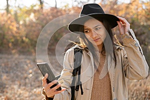 Stylish woman in hat captures the moment with selfie on smartphone walking at park with orange leaves