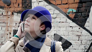 Stylish woman in hat closeup speak phone against background street graffiti 4K.