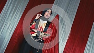 Stylish woman in hijab posing with red drapery background for a fashion shoot
