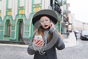 A stylish woman listens to music in the headphones on the background of a beautiful old town