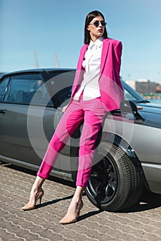 Stylish woman in a pink suit waiting near classic car