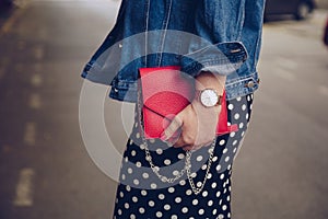 Stylish woman in polka dot culottes and denim jacket holding a red purse and wearing a rose gold wrist watch.