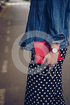 Stylish woman in polka dot culottes and denim jacket holding a red purse and wearing a rose gold wrist watch.