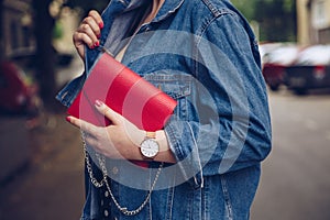 Stylish woman in polka dot culottes and denim jacket holding a red purse and wearing a rose gold wrist watch.