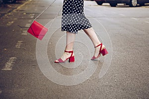 Stylish woman in polka dot culottes and red high heel shoes holding a red purse and crossing the road. street style fashion