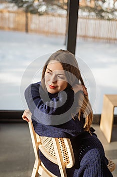 Stylish woman in a private house barnhouse wrapped herself in a warm knitted suit. Behind panoramic windows winter photo