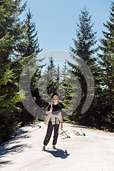 Stylish woman in roe deer clothes stands on a snowy trail in the mountains on a sunny spring day while walking in a mountain