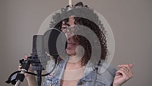 Stylish woman singer or musician sings a song into a microphone in a recording studio. Portrait of a creative person