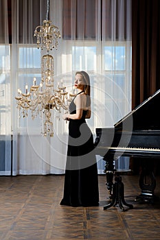 Stylish woman in sleeveless dress near grand piano