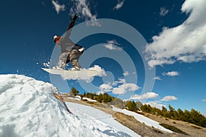 Stylish woman snowboarder makes a trick in flight. Snowboard jump from a kicker against the backdrop of mountains