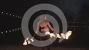 Stylish woman spinning burnign fans near at night