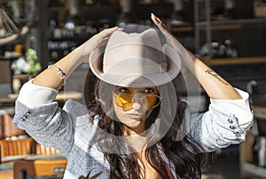 Stylish woman in sunglasses putting a hat on her head while sitting in a coffee shop