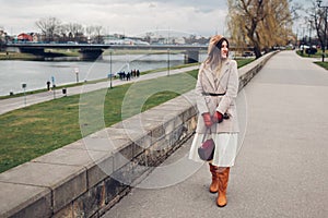 Stylish woman tourist walking along pier by Wisla river in Krakow, Poland enjoying landscape. Europe spring trip