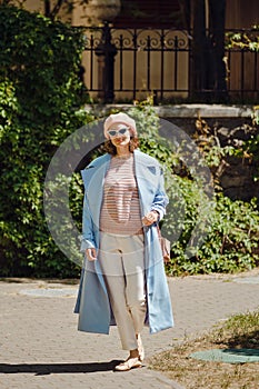 Stylish woman in trench coat, trousers and beret walking in old town