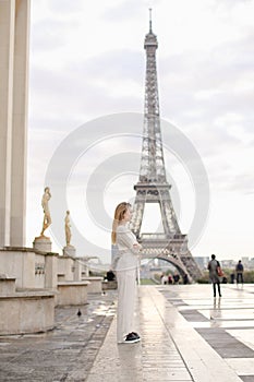 Stylish woman walking on Trocadero square near gilded statues and Eiffel Tower.