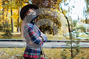 Stylish woman wears protective mask outdoors during coronavirus covid-19 pandemic. Girl walking in autumn park