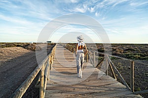 Stylish woman in white hat walking on the wooden promenade on the sea shore, relaxing , enjoying sunny day