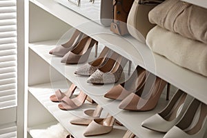 Stylish women`s shoes, clothes and bags on shelving unit in dressing room photo