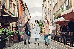 Stylish women walking on city street. Three girlfriends having fun in Lviv outdoors. Autumn fashion