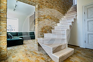 Stylish wooden contemporary staircase inside loft house interior. Modern hallway with decorative limestone brick walls and white