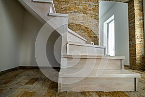 Stylish wooden contemporary staircase inside loft house interior. Modern hallway with decorative limestone brick walls and white