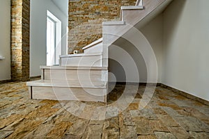 Stylish wooden contemporary staircase inside loft house interior. Modern hallway with decorative limestone brick walls and white