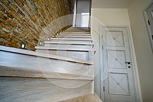 Stylish wooden contemporary staircase inside loft house interior. Modern hallway with decorative limestone brick walls and white