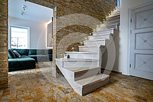 Stylish wooden contemporary staircase inside loft house interior. Modern hallway with decorative limestone brick walls and white