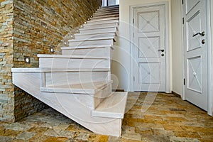 Stylish wooden contemporary staircase inside loft house interior. Modern hallway with decorative limestone brick walls and white