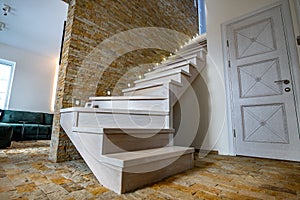 Stylish wooden contemporary staircase inside loft house interior. Modern hallway with decorative limestone brick walls and white