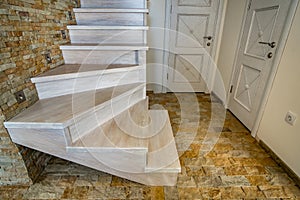 Stylish wooden contemporary staircase inside loft house interior. Modern hallway with decorative limestone brick walls and white