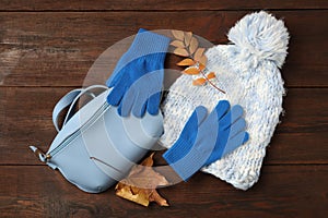 Stylish woolen gloves, hat, fanny pack and dry leaves on wooden table, flat lay