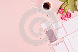 Stylish working space with flowers tulips, coffee cup, phone and blank white stationery on pastel soft pink background, copy space