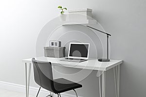 Stylish workplace with laptop and chair near white wall indoors. Interior design