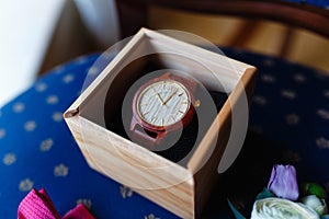 Stylish wristwatch in a wooden box. In background Pink bow tie, beautiful glass cufflinks, flower boutonniere. A men's set of acc