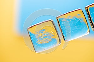 Stylish yellow and blue background with transparent ice-like cubes for drinks. Flat lay macro photo