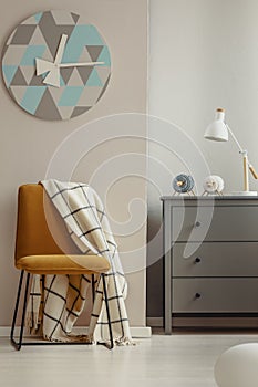 Stylish yellow chair in elegant interior with grey wooden chest of drawers