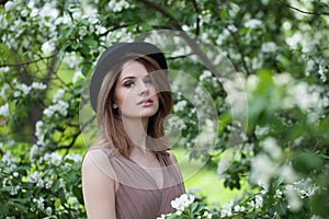 Stylish young adult woman female model with clean fresh skin, make-up and brown hair in blossom garden on green leaves background