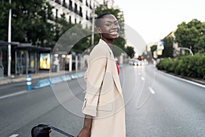 Stylish young adult woman looking at camera and smiling while crossing the street in the city