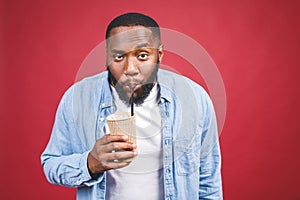 Stylish young african american man holding cup of take away coffee isolated over red background